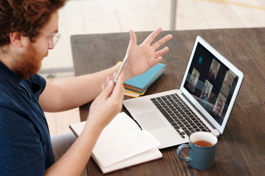 Man engaged in a virtual meeting at home with laptop and tea, chatting and studying online.