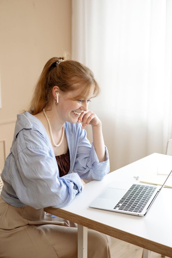 Learn English Online - A1/A2 Elementary Level Smiling woman learning English on her laptop at home, dressed casually.