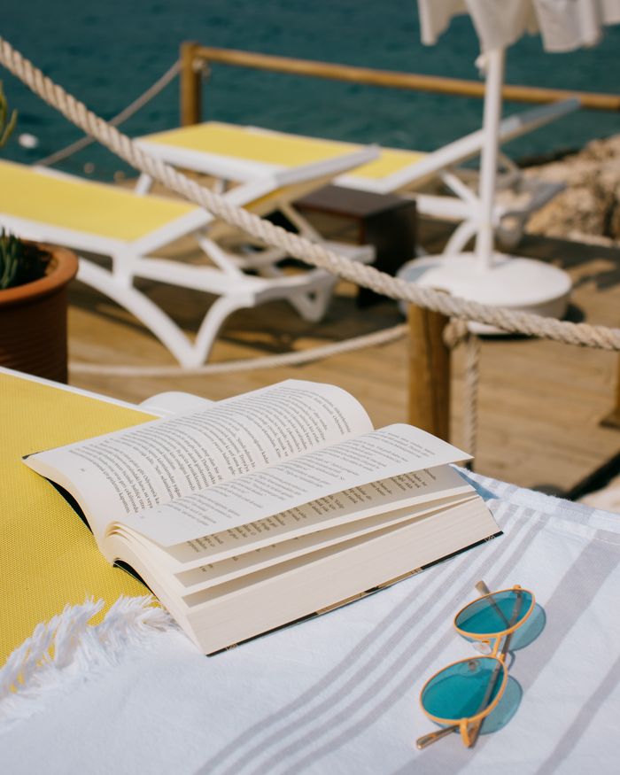 Summer Sun Discount! Open book and sunglasses on a towel by sun loungers at the beach.