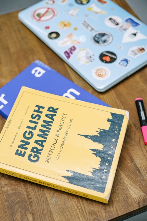 Mastering Singular and Plural Irregular Nouns High-angle view of an English grammar book and a laptop with stickers on a wooden desk.